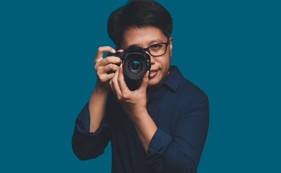 A Photographer holding a digital camera while standing on a blue background photo