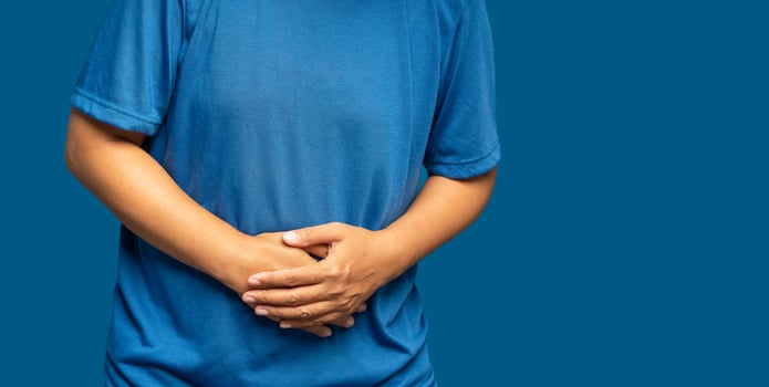 A young woman suffering from abdominal pain used her hand to hold her belly while standing on a blue background photo