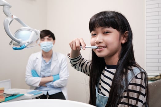 Portrait of an Asian girl demonstrates teeth brushing to pediatric dentist with toothbrush in dental clinic with happy smile, mouth dentistry hygiene, and orthodontic healthcare work in kid hospital. photo