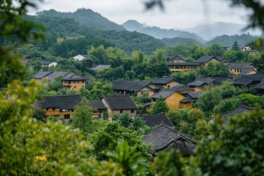 Hillside village with traditional houses nestled among lush green foliage and mountains under an overcast sky. photo