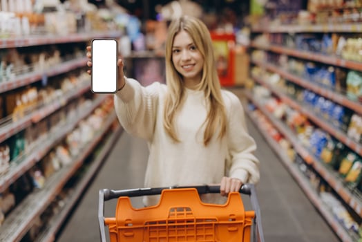 Woman showing smartphone with empty screen in supermarket photo