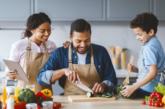 A loving African American family prepares a meal in their modern kitchen. The father chops vegetables as the mother and son assist, sharing smiles and laughter in a nurturing environment. photo