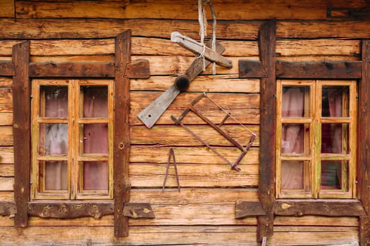 An old wooden wall of a house with windows in the village and tools hanging photo