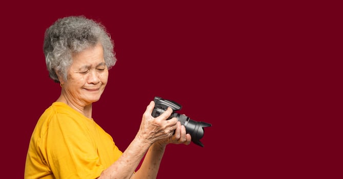 Happy senior woman looking at her photos in a digital camera while standing on a red background