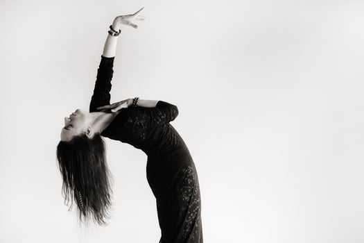 A girl in a black dress moves in a dance on a gray background. Dynamic dance photo