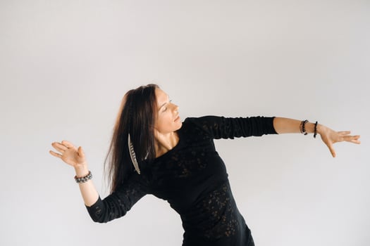 A girl in a black dress moves in a dance on a gray background. Dynamic dance photo