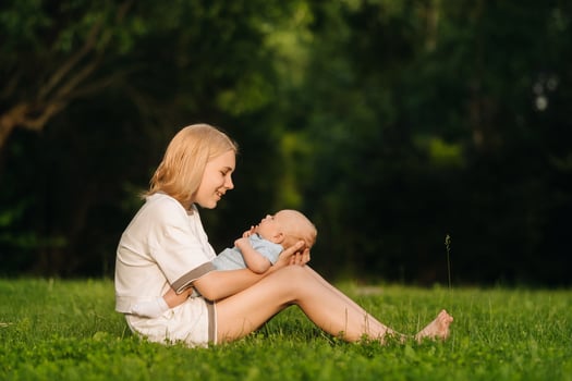 A mother holds a happy baby boy in her arms in a summer park photo