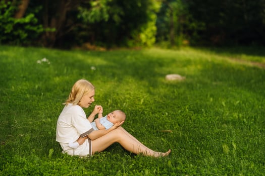 A mother holds a happy baby boy in her arms in a summer park photo