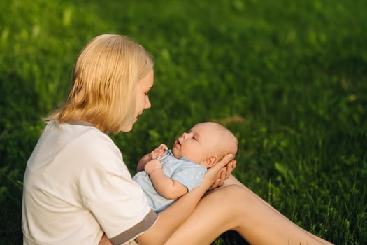 A mother holds a happy baby boy in her arms in a summer park photo