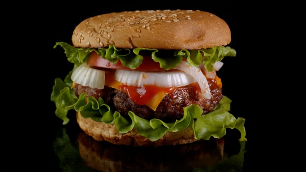 Big appetizing burger with fresh tomatoes, onions, juicy grilled beef patty and cheese. Fast food, Close-up photo