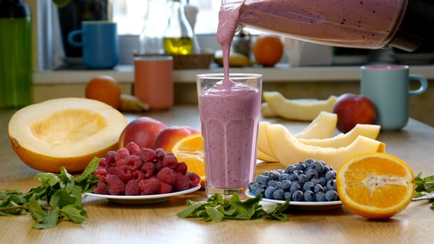 Raspberry Blueberry Melon Smoothie is poured into a glass on the background of fresh fruits and berries. The fruit cocktail is ready to eat. Healthy and vegetarian food concept photo