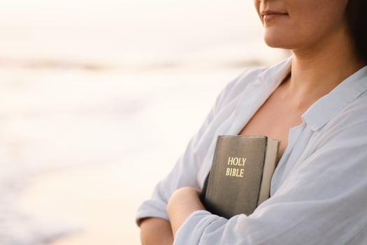 Christian woman holds bible in her hands. Reading the Holy Bible on the sea during beautiful sunset photo