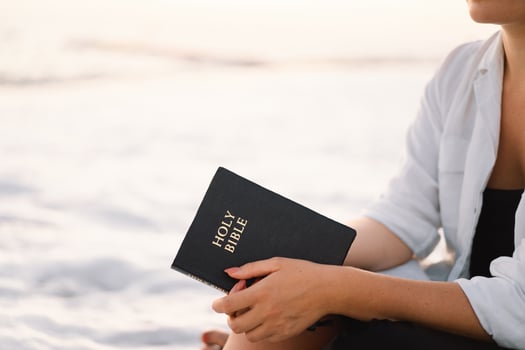 Christian woman holds bible in her hands. Reading the Holy Bible on the sea during beautiful sunset photo