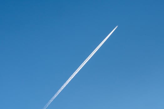 A jet leaves a long white contrail against a bright blue sky, creating photo