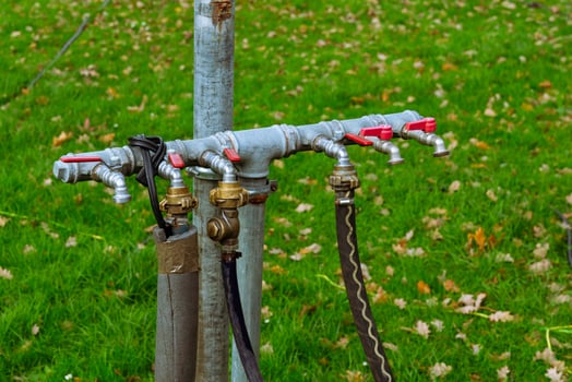 Several hose connections are attached to a metal pole in a grassy area photo