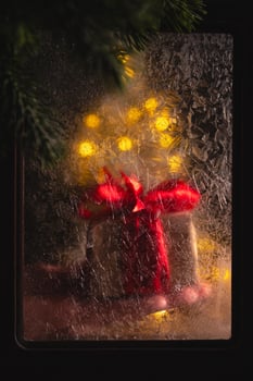 Hand is placing a christmas gift wrapped in red paper behind a frosted glass pane, with warm christmas lights twinkling in the background, creating a festive and magical atmosphere photo
