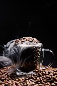 Glass cup overflowing with coffee beans and emitting smoke on a black background photo