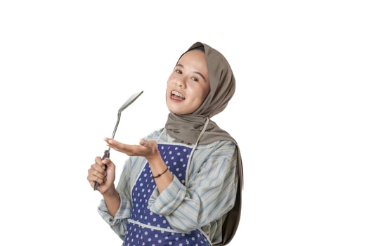 A cheerful woman wearing a hijab and apron is holding a spatula, ready to cook up something delicious in the kitchen. photo