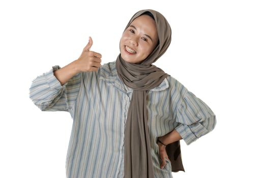 A cheerful woman wearing a hijab and a striped shirt gives a thumbs-up gesture while smiling, radiating positivity and confidence. photo