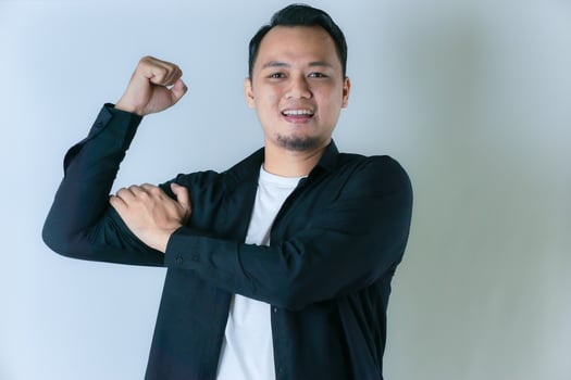 A man in a black shirt poses in a triumphant gesture, stretching his arms and showing joy, against a plain background. photo