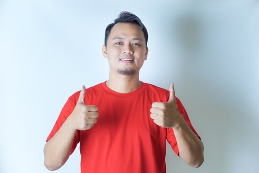 A man in a red shirt is smiling and giving two thumbs up, showing a gesture of positivity and approval against a plain white background. photo