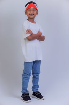 A young boy in a white shirt, blue jeans, and a red-white headband stands confidently with folded arms. photo