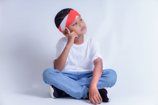 A thoughtful child wearing a red and white headband, sitting cross-legged in a white t-shirt and jeans. photo