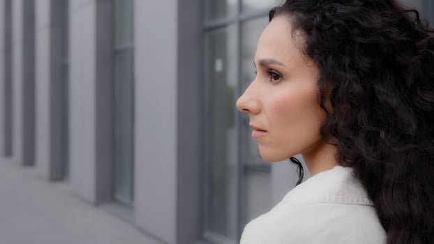 Close up back view Caucasian pensive thoughtful brunette lady with long curly hair looking away thinking dreaming pondering think waiting standing outdoors in city calm Latina Hispanic woman outside photo