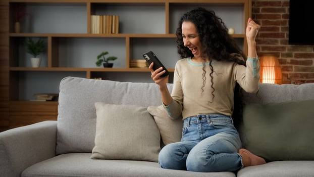 Happy woman lady using phone for bet in internet receive message with good news offer sitting on couch at home win mobile phone win game online victory virtual app success winning triumph celebrate photo