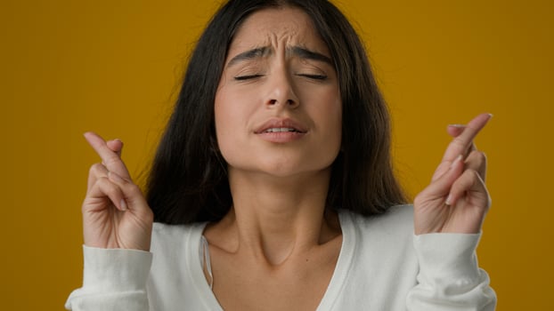 Close up portrait in studio yellow background Indian ethnic woman girl lady female makes wish crosses fingers for good luck waits wish pray wishing paring about win victory success help beg dreaming photo