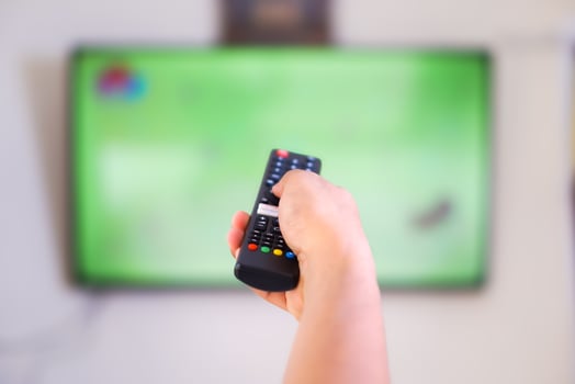 A hand holding a remote control aimed at a television photo