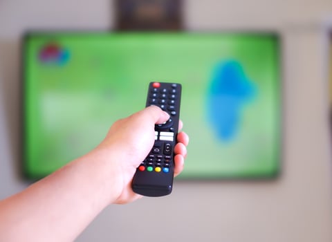 A hand holding a remote control aimed at a television photo