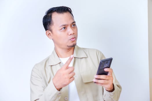 A man holding a phone looks surprised while raising his finger in thought. photo