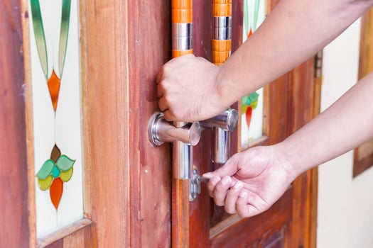 A hand unlocking a wooden door with decorative glass panels and modern handles. photo