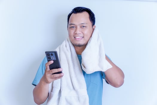 An Asian man in a towel smiling while checking his phone, exuding happiness and relaxation. photo