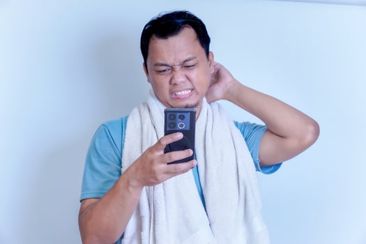 Frustrated man checking his phone, deep in thought, with a towel around his neck photo