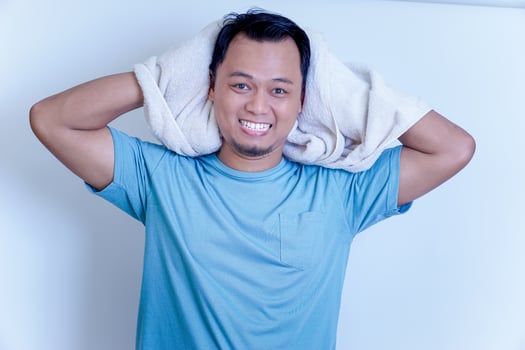 A young Asian man smiling confidently after shower , holding a towel over his shoulder in a bright setting. photo