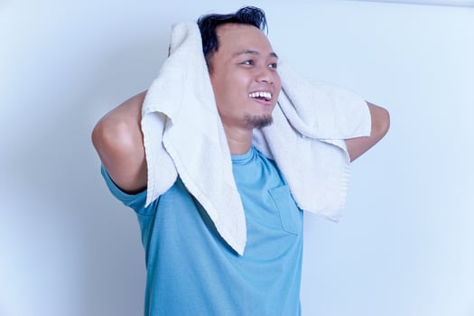 A young Asian man smiling confidently after shower , holding a towel over his shoulder in a bright setting. photo