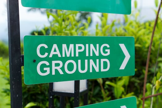 A green sign directing visitors to the camping ground, surrounded by greenery. photo
