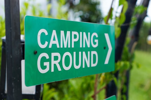 A green sign directing visitors to the camping ground, surrounded by greenery. photo