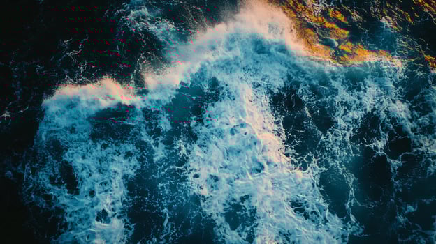 The ocean is rough and choppy, with waves crashing against the shore. The water is a deep blue color, and the sky is a dark blue. Scene is one of power and energy photo