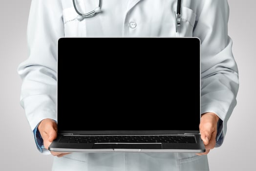 Online consultation. Woman doctor in white coat and with stethoscope holds laptop in her hands and shows blank screen, close up photo
