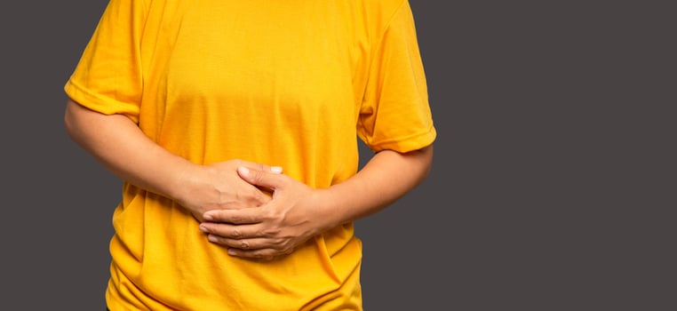 A woman suffering from abdominal pain used her hand to hold her belly while standing on an orange background photo