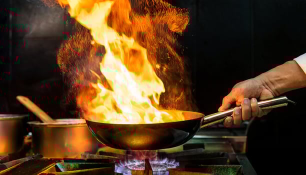 close-up of a chef hands holding a pan with dramatic flames rising in a high-energy professional kitchen scene photo