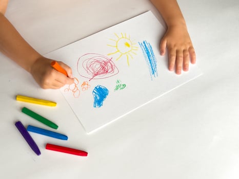 Child drawing with colorful crayons on white paper photo