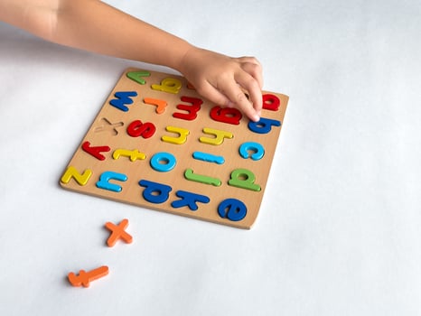 Childs hand arranging colorful alphabet puzzle on wooden board for early learning photo
