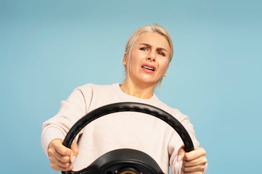 Scared woman driving with steering wheel on blue background photo
