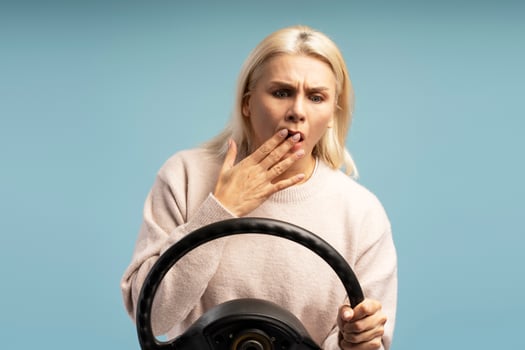 Shocked woman holding steering wheel on blue background photo
