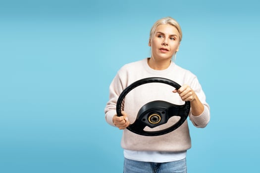 Woman holding steering wheel, simulating driving a car on blue background photo