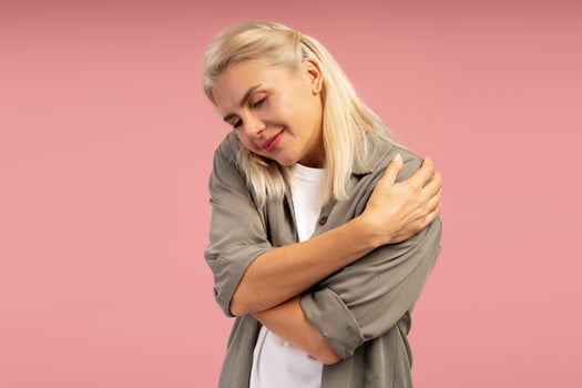 Blond woman hugging herself on pink background showing self love and acceptance photo